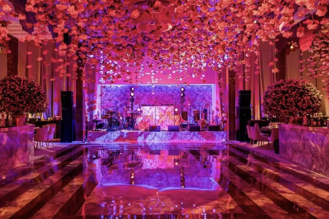 A vibrant event space features a ceiling adorned with colorful flowers, a glowing stage, and a reflective marble floor, creating a festive ambiance.